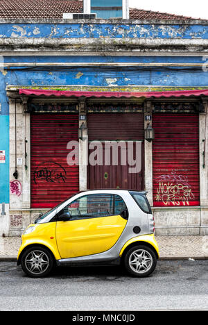 Gleaming new yellow and silver smart fortwo car parked in front of dilapidated shuttered shop Stock Photo