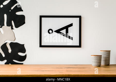 Modern poster with a horizontal letter on the white wall, above wooden desk with two porcelain containers Stock Photo