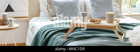 Close-up panorama of a wooden breakfast tray with cookies and coffee mugs on a cozy bed in bright bedroom interior Stock Photo