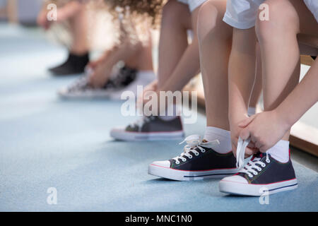 Close-up on school kids' legs while they're sitting on a bench and tying their sport shoes for physical education activities Stock Photo