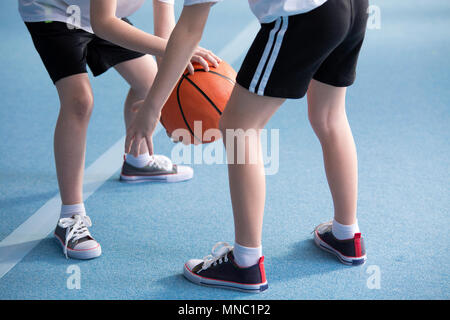 Close-up on young children wearing school sportswear learning to dribble a basketball during physical education classes in gym with blue floor Stock Photo