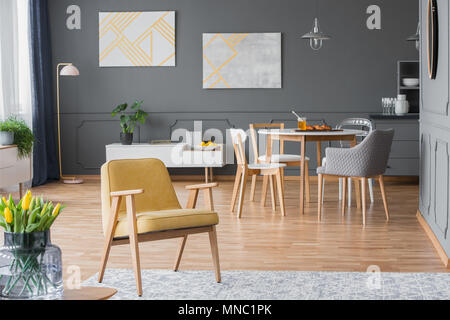 Vintage, yellow armchair in a dining room interior with a round table, chairs and paintings Stock Photo