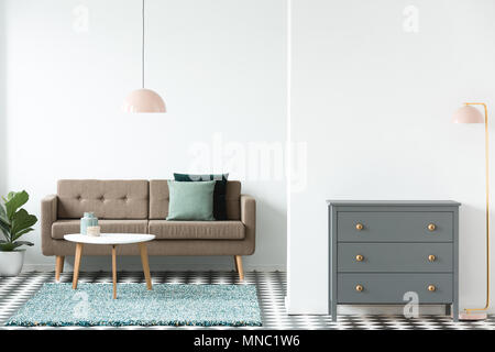 Pink lamp next to grey cabinet in retro living room interior with white table on rug near brown sofa Stock Photo