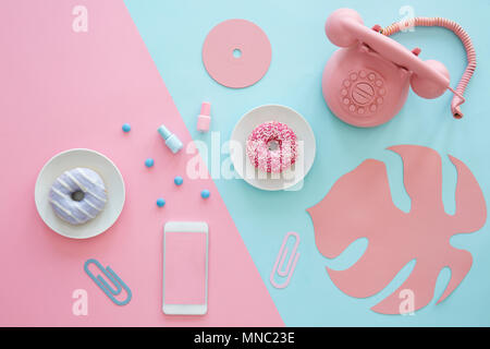Pink and blue table top of a blogger with a phone, donuts, paper leaf and cd Stock Photo