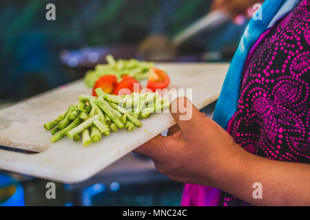 Raw chopped vegetables ready for cooking on a chopping board with a holding hand of a woman. Stock Photo