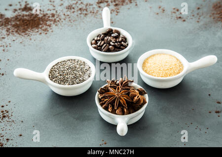 Coffee beans, seeds and star anise in small, matching bowls on a gray table. Concept of flavoring food Stock Photo