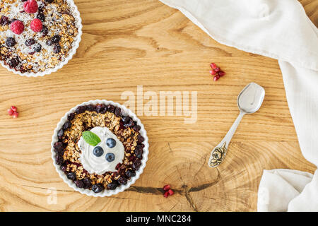 Top view of a wooden breakfast table with two bowls of oatmeal with fruit, elegant silver spoon and white cloth Stock Photo
