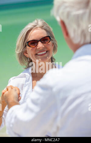 Happy senior man and woman couple dancing and holding hands on a deserted tropical beach with turquoise sea and clear blue sky Stock Photo