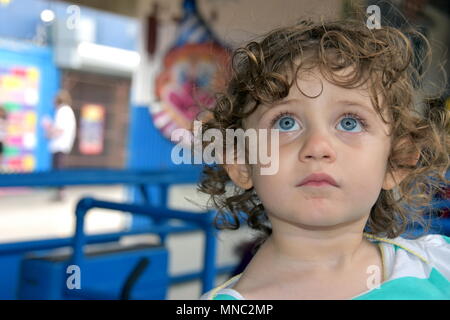 Beautiful little girl stares up at an amusement park ride while waiting below in the line Stock Photo