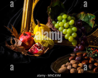 Still life with fresh fruit and dried fruit. Grapes, pomegranate, yellow melon, yellow squash, walnuts, chestnuts. Black background. Golden picture fr Stock Photo