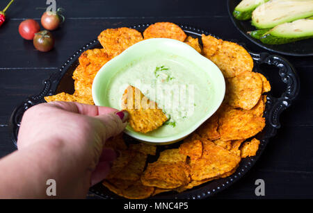 Hand dipping tortilla chips into green dip on a plate Stock Photo