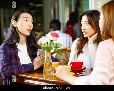 three happy beautiful young asian women sitting at table chatting talking in coffee shop or tea house. Stock Photo