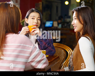 three happy beautiful young asian women sitting at table chatting talking in coffee shop or tea house. Stock Photo