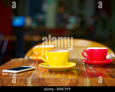 three cups of cappuccino and a cellphone on table in a coffee shop Stock Photo