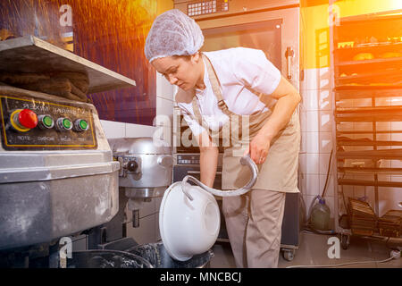 Young woman baker in white uniform works, washes large basin in bakery Stock Photo