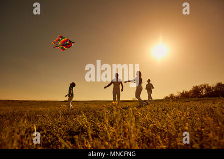 Happy family with a kite playing at sunset in the field Stock Photo