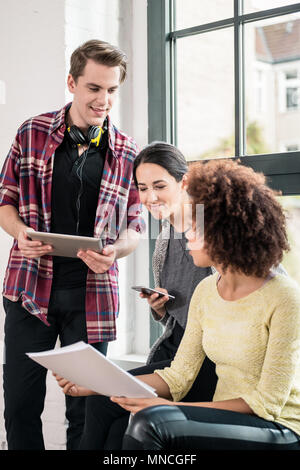 Three young employees using modern devices during break Stock Photo