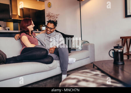 Cheerful interracial couple sitting on a couch in living room. Man relaxing with girlfriend on a sofa and smiling. Stock Photo