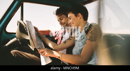 Couple looking at a map sitting in car. Smiling man and woman using map to navigate on a road trip. Stock Photo