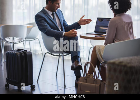 Business man showing something to woman while sitting at airport lounge. Business people working on laptop while waiting for their flight. Stock Photo