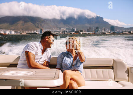 Cheerful young couple sitting on a boat. Young man and woman sitting at the back of the yacht and laughing. Stock Photo