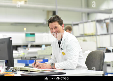 portrait of a friendly worker/ engineer in a modern factory at the desk - industrial fabric for  assembly of electronics products Stock Photo