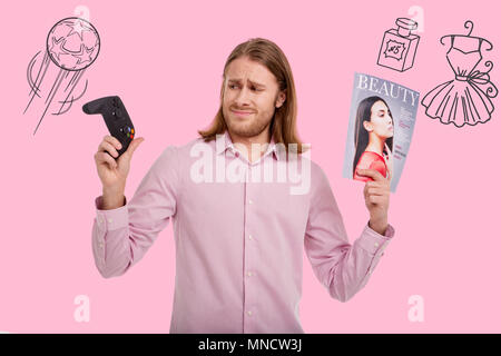 Worried man frowning while choosing between a men game and a women magazine Stock Photo