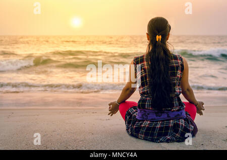 A millennial young adult meditating on the beach Stock Photo