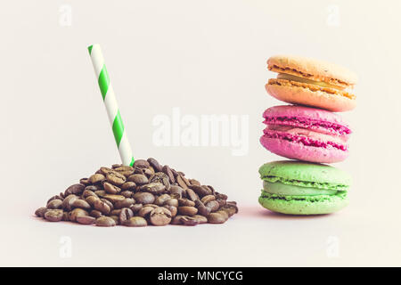 Pile of coffee beans with drinking straw and colorful macaroons on pastel pink background. Stock Photo