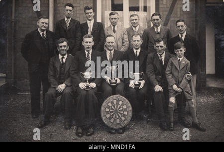 Vintage Photograph of a Public House Darts Team With Their Trophies and Dartboard Stock Photo