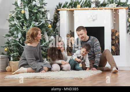 Happy family sitting on rug by Christmas tree at home Stock Photo