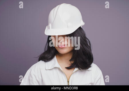 Young female construction worker wearing hardhat against purple background Stock Photo