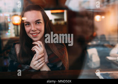 Smiling beautiful young woman seen through cafe window Stock Photo