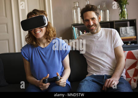 Portrait of smiling man sitting by woman playing on virtual reality headset in living room at home Stock Photo