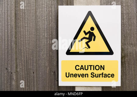 CAUTION uneven surface sign black and yellow warning triangle with man slipping and falling on wooden fence Stock Photo