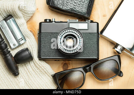 Accessories of the creative person. 35-mm film camera, exposure meter in leather case, steel flask, sunglasses and smoking set on wooden background. Stock Photo