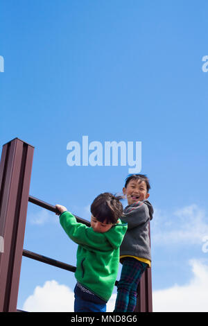 Low angle view of boys climbing on playground equipment against blue sky Stock Photo