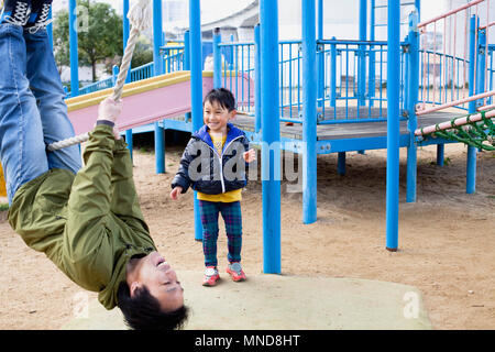 Smiling boy looking at father swinging on rope in playground Stock Photo