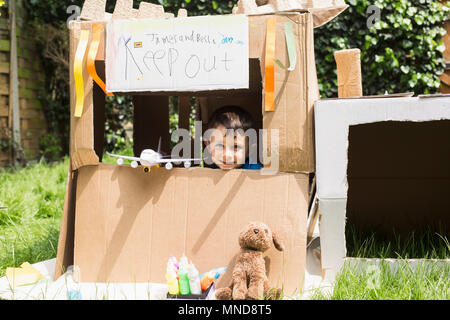 Portrait of cute boy with toys in cardboard playhouse at back yard Stock Photo