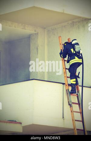 Firefighter with oxygen cylinder climbing a wooden ladder  with vintage old effect Stock Photo