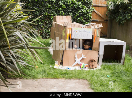 Boy in cardboard playhouse with toys at back yard Stock Photo