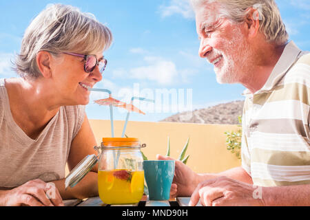 Senior couple drink from a vase a fruit juice with strawberry. Together on a terrace with blue sky in background. Stock Photo