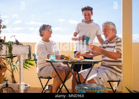 family of different ages with grandparents and grandson spend free time on the terrace eating and drinking on an outdoor terrace in summer Stock Photo