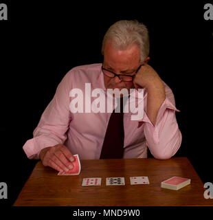 Elderly man with grey hair looking unhappily at his poker hand image with copy space against a black background Stock Photo