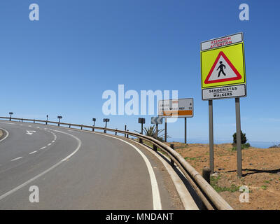 Footpath on a sharp bend of a major coastal road in northern La Gomera Canary Islands with clear pedestrian warning sign Stock Photo