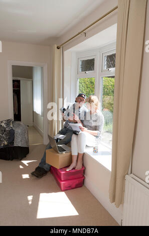 Moving house. Couple sitting on a window seat viewing and checking an account to be settled before completion of the sale. Stock Photo
