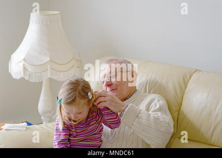 A grandfather adjusting the hairclips of his thre year old grand-daughter Stock Photo