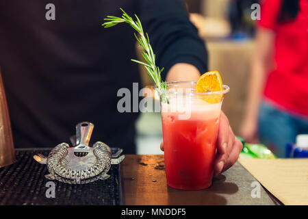 Expert pro barman hands representing cocktail in plastic glass decorated with fresh rosmarineand dried orange. Drinking cocktails, nightlife and party Stock Photo