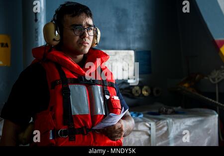 180515-N-OY799-0210 WATERS SOUTH OF JAPAN (May 15, 2018) Boatswain's Mate Seaman Yoshua Nunez, from Orlando, Florida, mans a sound-powered telephone in the hangar bay aboard the Navy's forward-deployed aircraft carrier, USS Ronald Reagan (CVN 76), as part of a replenishment-at-sea with Military Sealift Command (MSC) dry cargo/ammunition ship USNS Cesar Chavez (T-AKE 14), during sea trials, May 15, 2018. The non-combatant, civilian-crewed ship, operated by MSC, provides fuel, food, ordnance, spare parts, mail and other supplies to Navy ships throughout the world. Ronald Reagan, the flagship of  Stock Photo