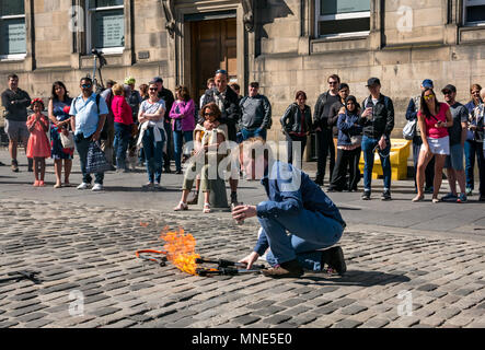 Royal Mile, Edinburgh, 16th May 2018. Tourists enjoying the sunshine and street entertainment on the Royal Mile, Edinburgh, Scotland, United Kingdom. Tourists watch a street performer called Daniel, whose act includes juggling flaming torches and large knives and machetes Stock Photo